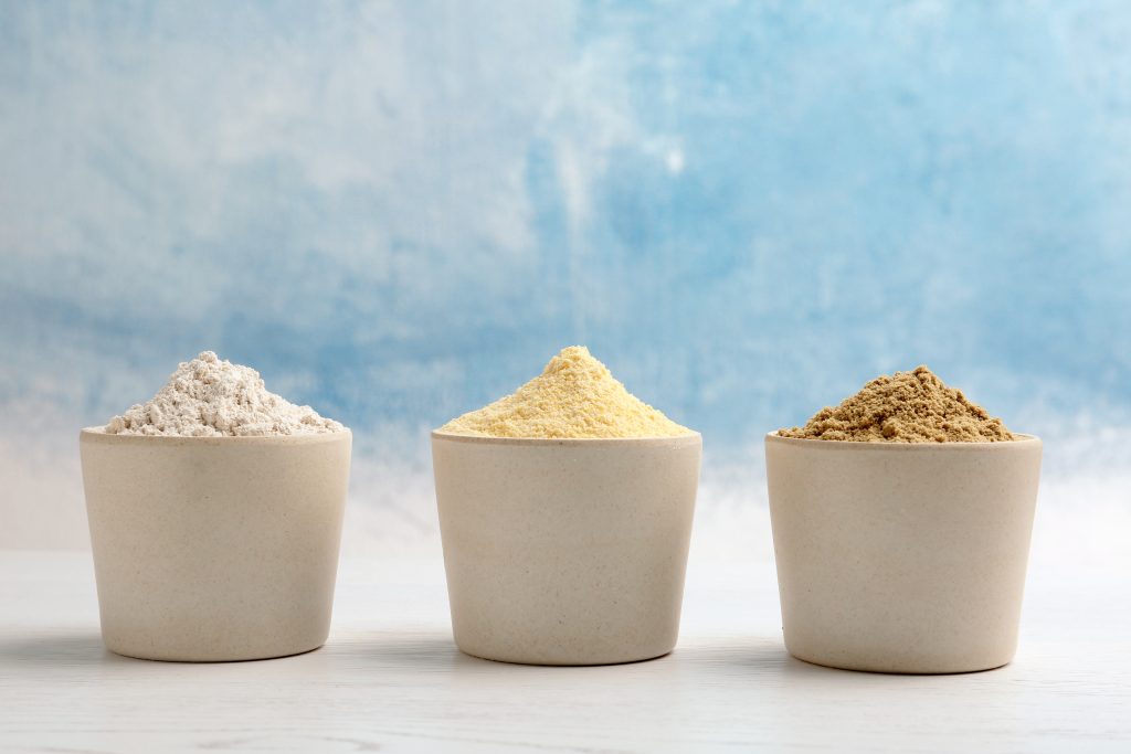 Three different types of flour against a blue and cloudy sky used to broadly represent the idea of looking for a protein powder. 