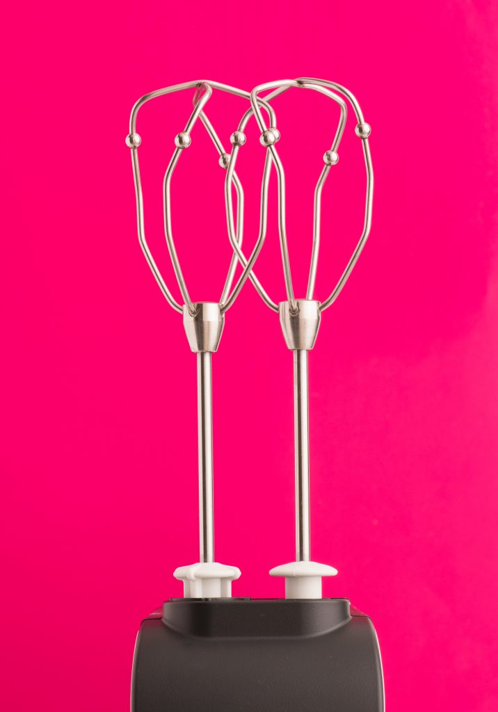 Close up of two twisted beaters used in a hand mixer pictured against a pink background.