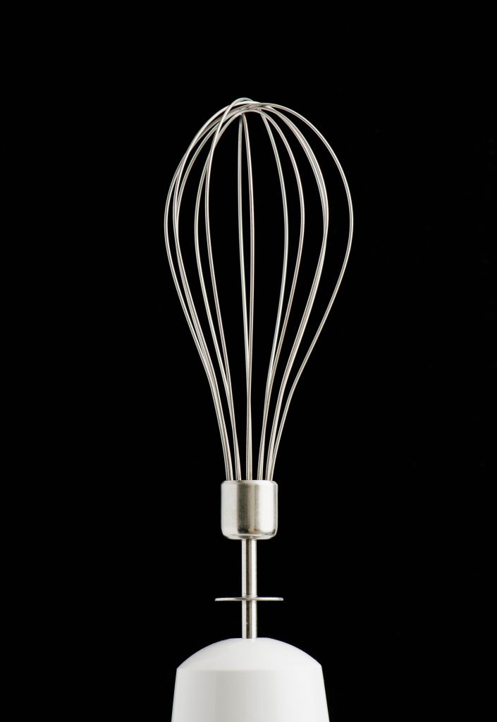 Close up of a whisk used in a hand mixer pictured against a black background.