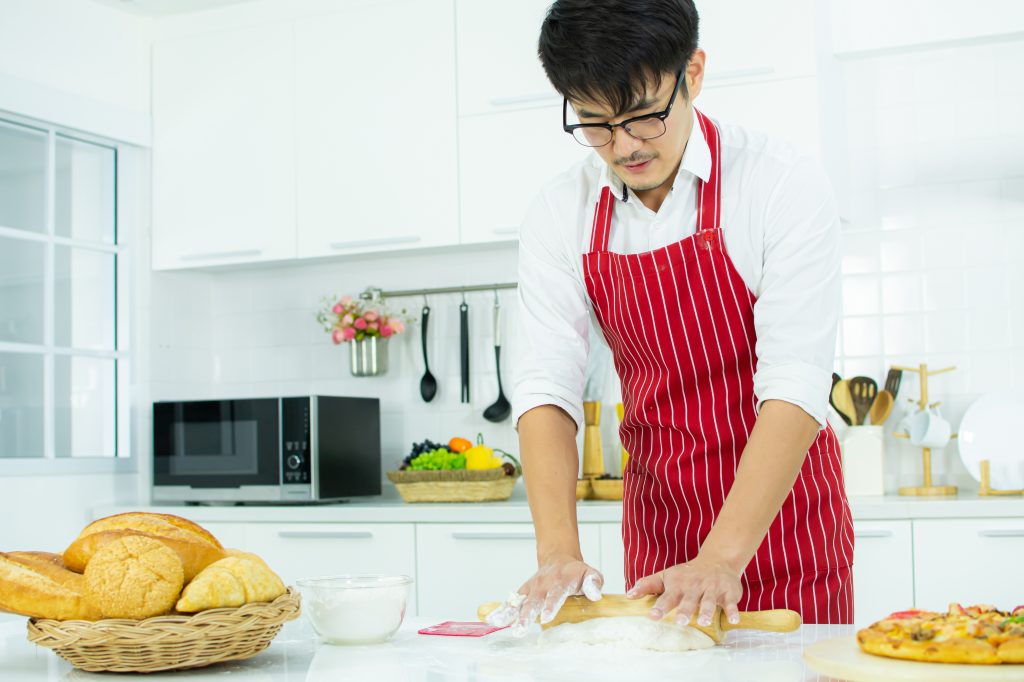 An Asian man working dough on a kitchen counter with a countertop oven in the background.