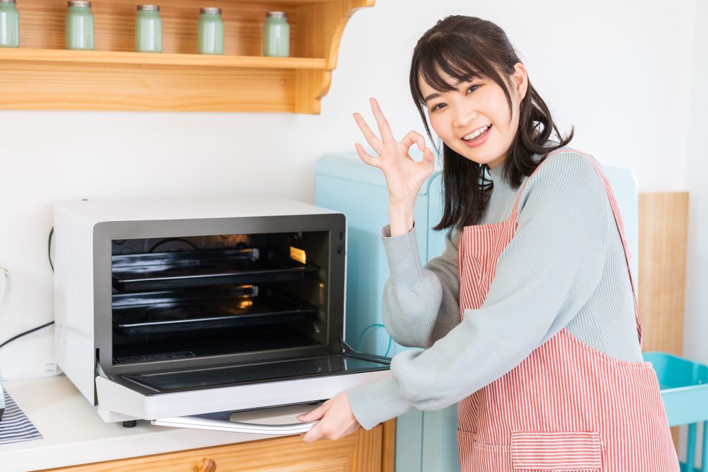 A Japanese woman in an apron opening the door of an oven very similar to the Sharp RE-SS10-XW Superheated Steam Oven.