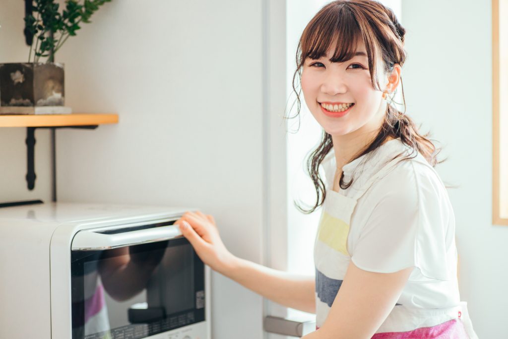 A Japanese women smiling with her hand on an oven door similar to the Iris Ohyama F30002 superheated steam oven.